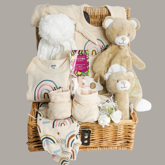baby hamper basket with baby organic clothing outfit in beige with rainbow , eco friendlt baby white bobble hat, organic booties, eco friendly teddy comforter and rattle, cocoba chocolate spoon