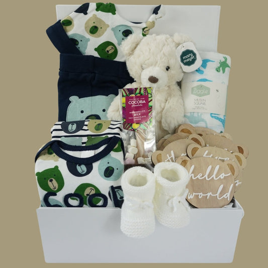 baby hamper with navy blue baby set including baby joggers and 2 baby vests and match hat, milestone wooden teddy discs , cocoba chocolate spoon with marshmallows, baby white knit booties, cream teddy, white muslin with blue and green dinosaurs