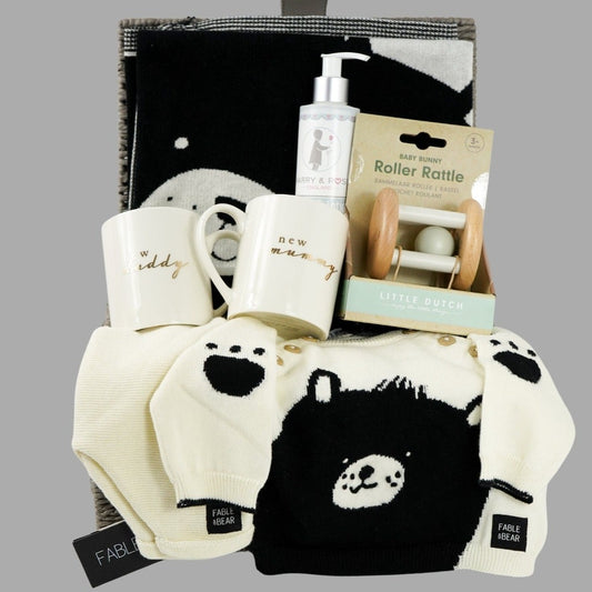 Neutral baby gift hamper, baby jumper in cream with black teddy face and matching cream joggers, New mummy and New daddy cream mugs with gold writing, wooden baby rattle, Black and cream teddy face baby blanket, organic baby lotion