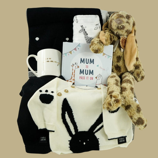 baby hamper with organic baby clothing set  in black and cream with bunny  face, matching black and cream organic cotton baby blanket with bunny face, white swaddle with  grey giraffes, cream porcelain mug with new mummy in gold lettering, leopard print fluffy bunny soft toy, mum advice and tips hard back book