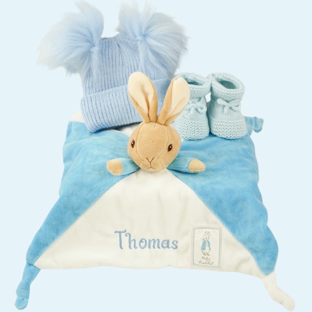 white hamper box with blue and white knot peter rabbit comforter, blue knit booties and blue hat with bobbles 