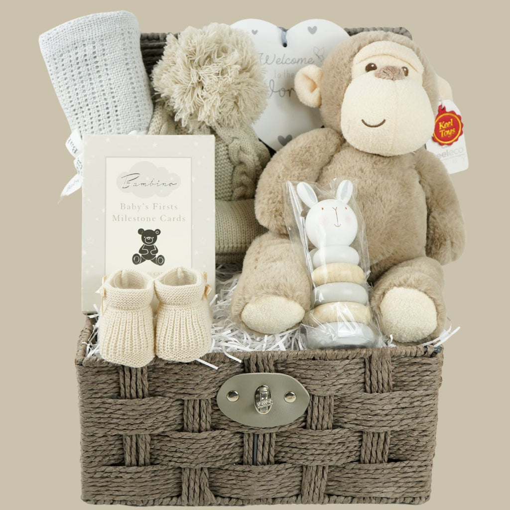 Baby grey hamper basket with grey cellular baby blanket, baby biscuit coloured pom pom hat, heart hanging nursery plaque, Baby milestone Cards, baby booties in biscuit colour, wooden stacking toy and soft eco friendly baby soft toy