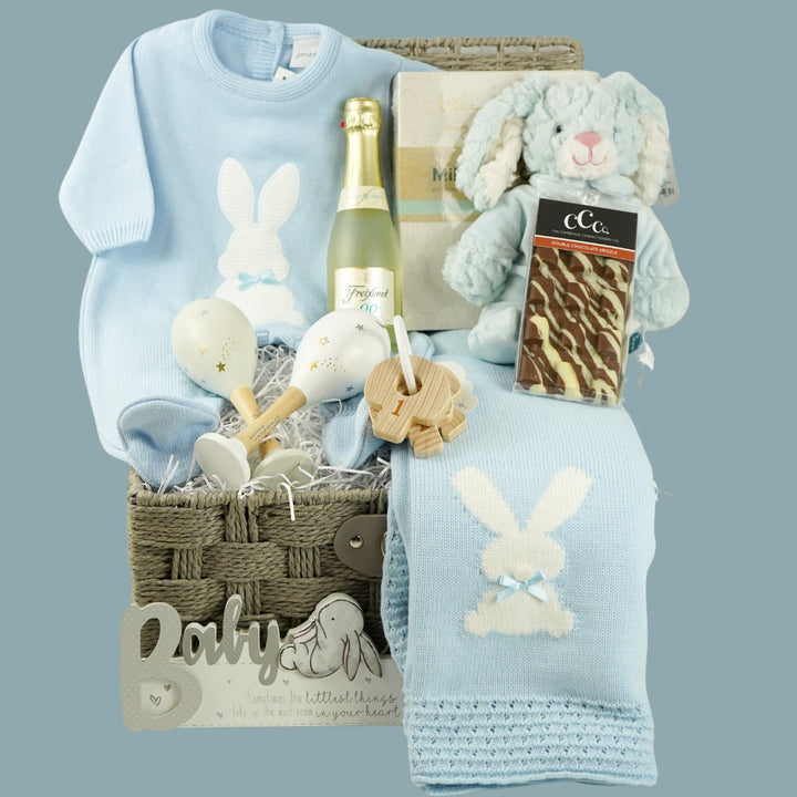 luxury baby and new parents hamper gift, blue baby blanket with white rabbit, knit blue romper with feet and white bunny, maracas, wooden teething key ring, small bottle of freixenet, chocolate, Little Dutch baby bunny milestone cards in a box, soft blue bunny in a velour pj's