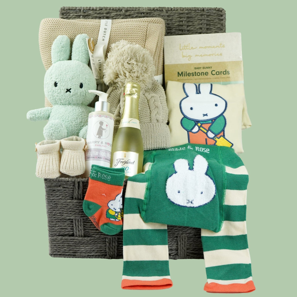 grey hamper baby basket with light green miffy, organic beige blanket, organic baby pompom hat, Little Dutch baby milestone cards, biscuit coloured nit booties, organic baby wash, mify organic clothing set includes a long sleeved tshirt, knit leggings with miffy on the bum, miffy socks , non alcoholic prosecco