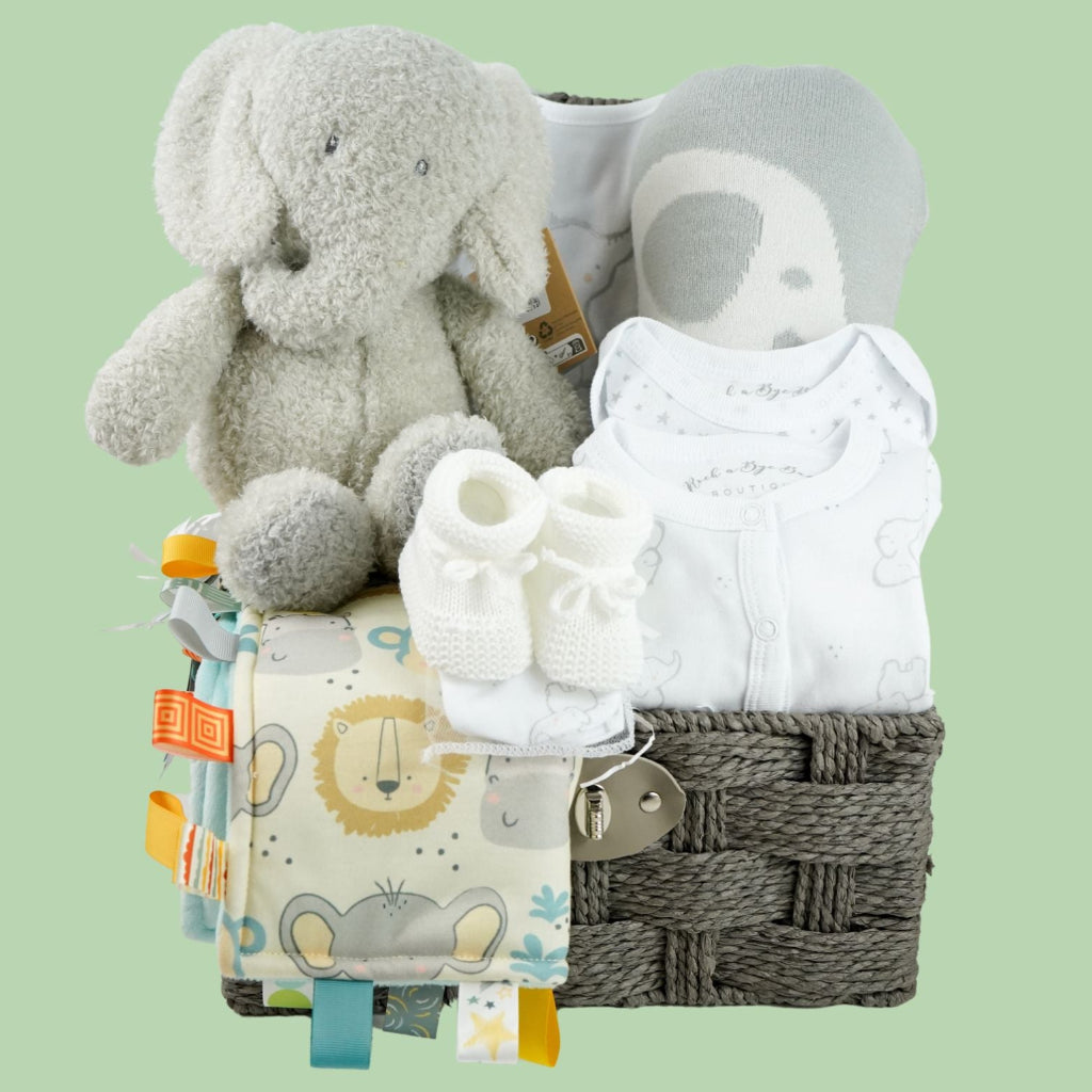 neutral baby hamper in grey rope basket, grey nattou soft elephant, grey and white soft baby blanket, taggie blanket with lion, elephants and zebras faces  with fleece backing, white baby layette set with grey elephant  design includes baby sleepsuit, baby bodysuit, hat, mittens and bib