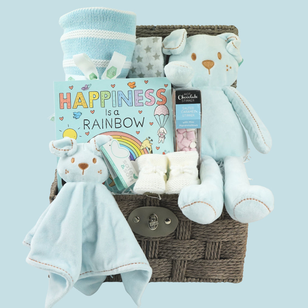 hamper basket with baby blanket in blue and white stipe, soft teddy dog in blue and matching comforter,  board boo, white knit booties and white muslin square 