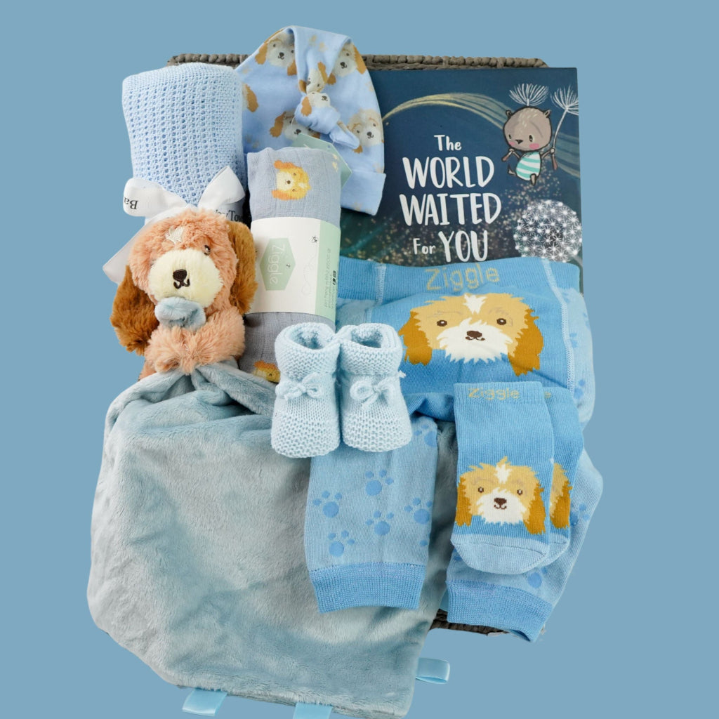 baby boy hamper box with blue puppy baby comforter with taggies, blue legging with a puppy on the bum, blue socks with puppy head, baby blue booties,  blue baby muslin with puppy, blue knot hat with puppy, blue cellular baby blanket, 'The world waited for you ' book