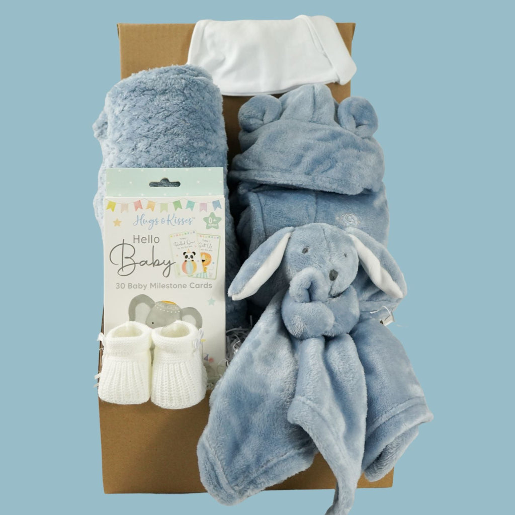 Baby gift set with blue blanket, booties, and comfort toy in a box on a light blue background