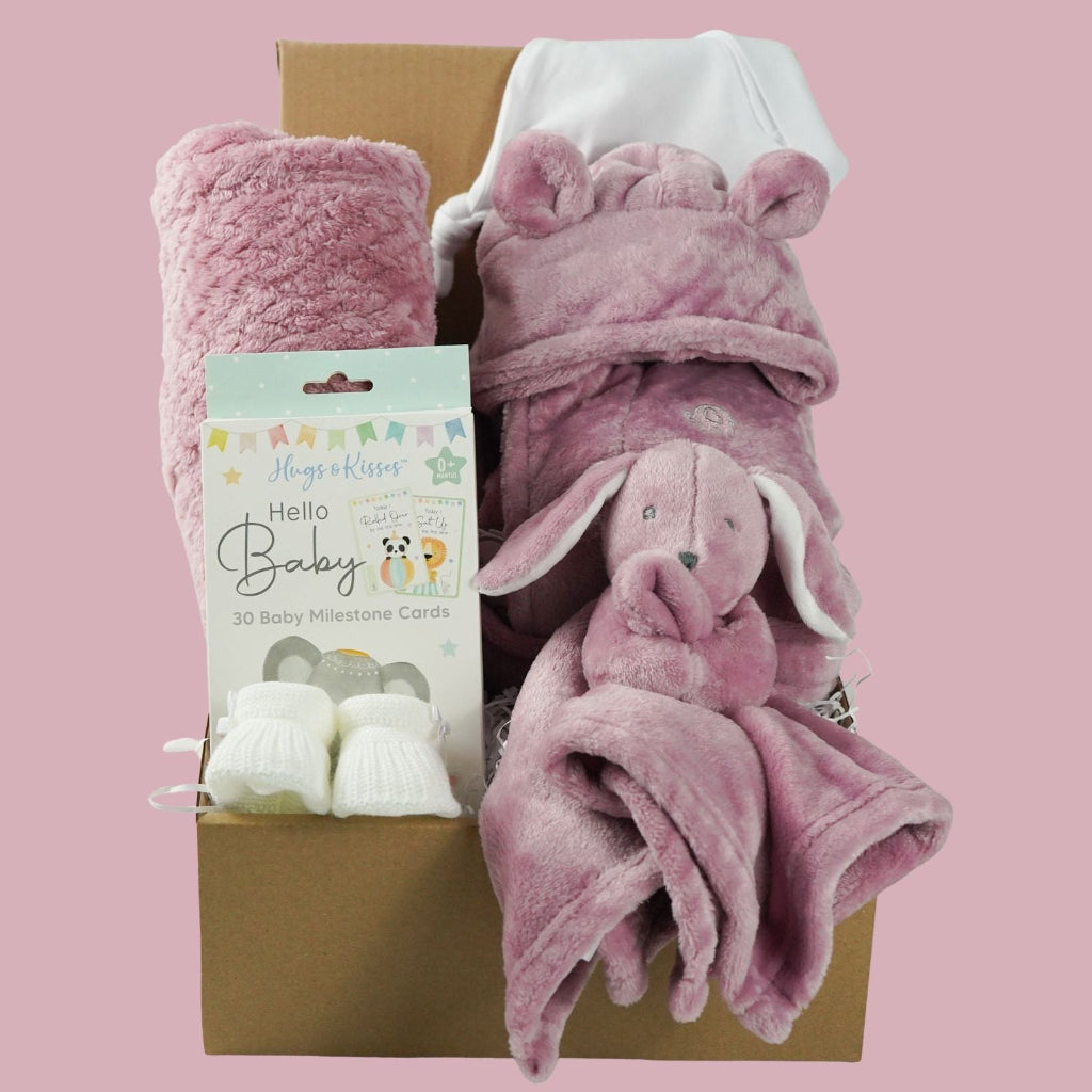 Baby gift set with pink plush baby comforter in pink with matching dressing gown and blanket all in a dusky pink fleece , baby white knot hat and white knit booties and baby milestone cards packaged in a  box