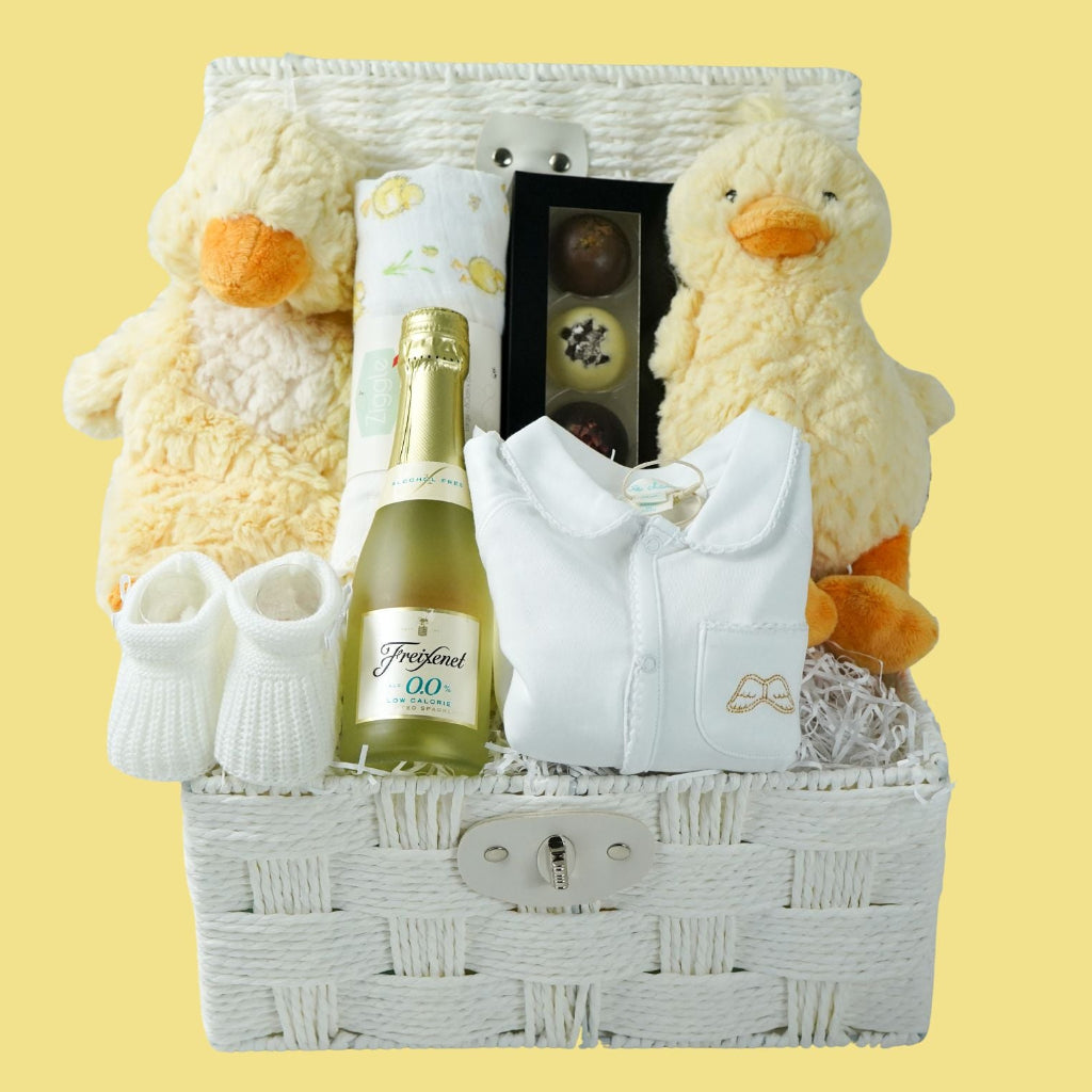 luxury baby gift hamper basket with yellow duck lovey and yellow duck , white muslin square with yellow ducks , white booties , luxury baby sleepsuit in white with gold angel wings embroidered on front  pocket and picot edging