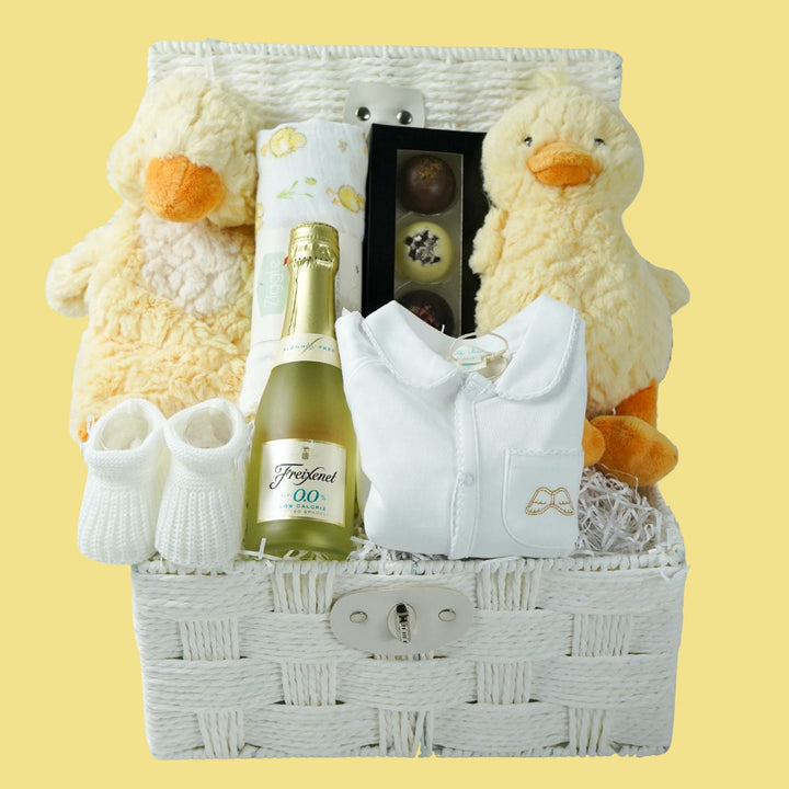 luxury baby gift hamper basket with yellow duck lovey and yellow duck , white muslin square with yellow ducks , white booties , luxury baby sleepsuit in white with gold angel wings embroidered on front  pocket and picot edging