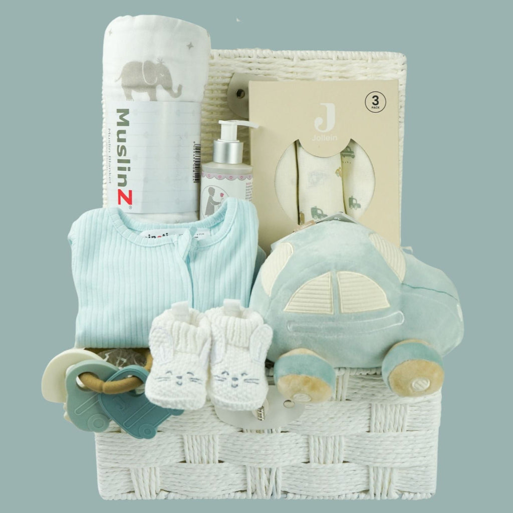 baby hamper with blue zip up baby sleepsuit, baby muslin basket in white with grey elephants, toiletries for baby, three muslins in cream with cards , car soft activity toy, white baby booties with rabbit face, silicon baby teether with 2 cars and keys in blues and cream