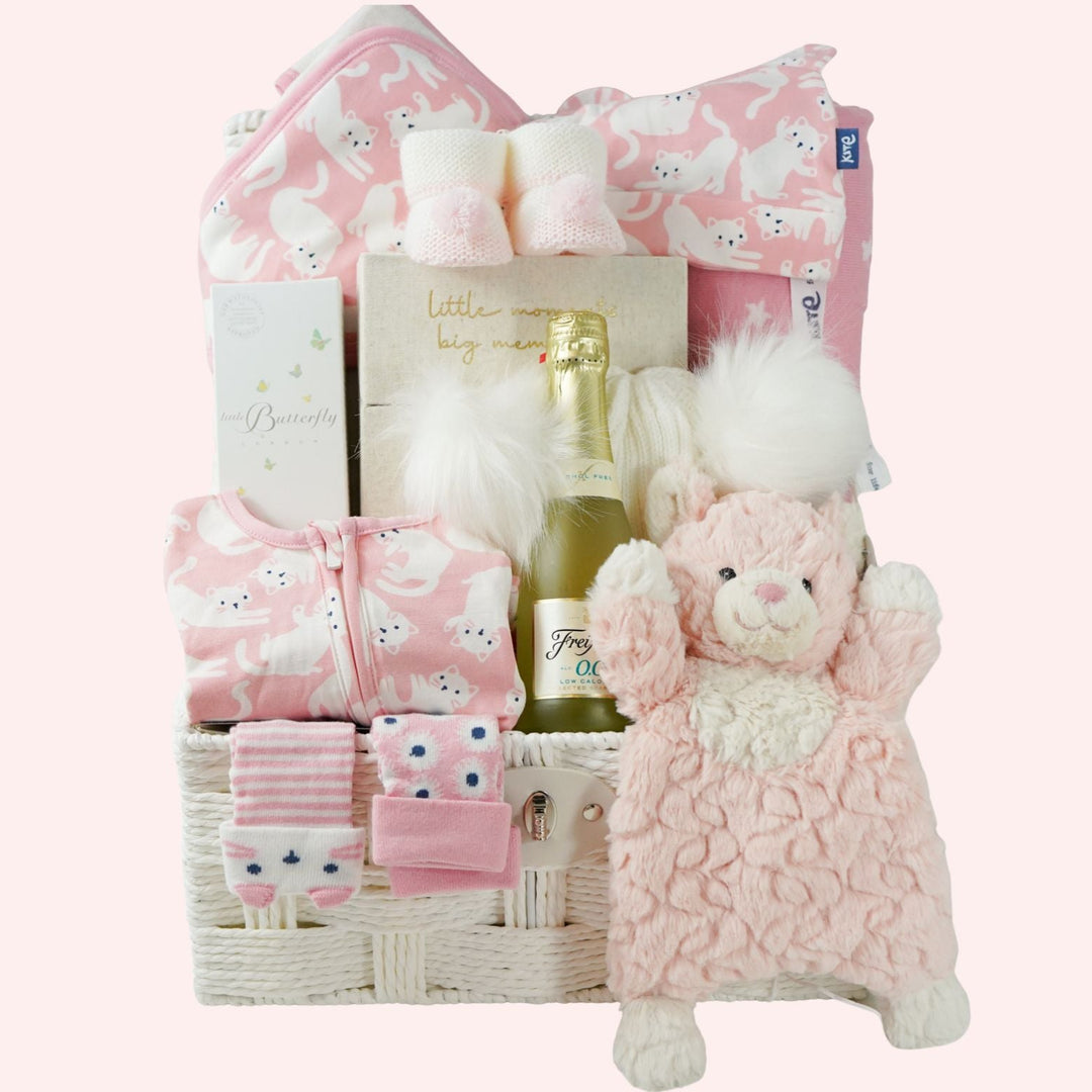 Baby gift basket with pink plush toy, pink organic baby clothes, baby pink wrap with kittens, pink organic baby blanket, milestone cards, organic body wash and bottlle of nonsecco 
