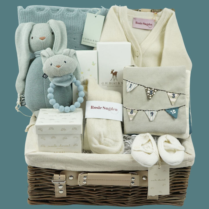 luxurry baby gifts in a wicker hamper with knitted luxury bunny and ring rattle, cashmere baby blanket, cashmere baby cardigan , luxury candle, luxury toiletries , cashmere baby slippers