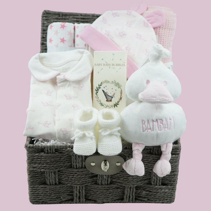 A baby gift basket set containing a white long-sleeve baby sleepsuit with pink mice a pink and white baby hat wih cute ears, white knit booties, a plush duck toy embroidered with 'BAMBAM, and a folded white blanket, all arranged in a dark gray wicker basket 