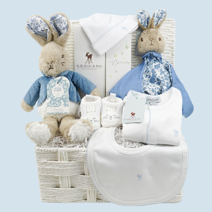 luxury baby gift hamper basket with peter rabbit soft toy, peter rabbit comforter, bunny slippers, luxury baby sleepsuit in white with blue picot edging and matching bib and hat, baby luxury hairbrush, organic baby toiletries 