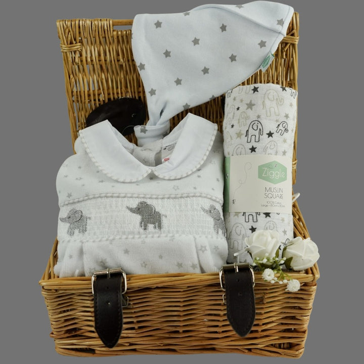 Small wicker basket, white velour baby sleepsuit with stars and grey elephants with a smocked front, white muslin with grey elephants, white cotton baby knot hat with silver stars 