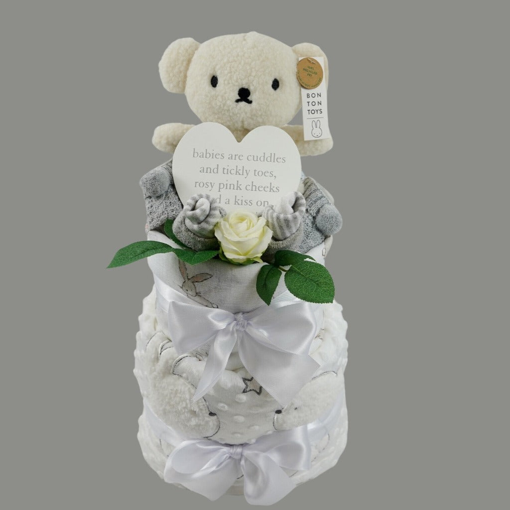 baby cake with grey striped socks, baby bootees in grey with pom poms, white dimpled blanket with sherpa backing with a bunny and teddy applique, white swaddle with bunnies, cream teddy , white plaque for the nursery