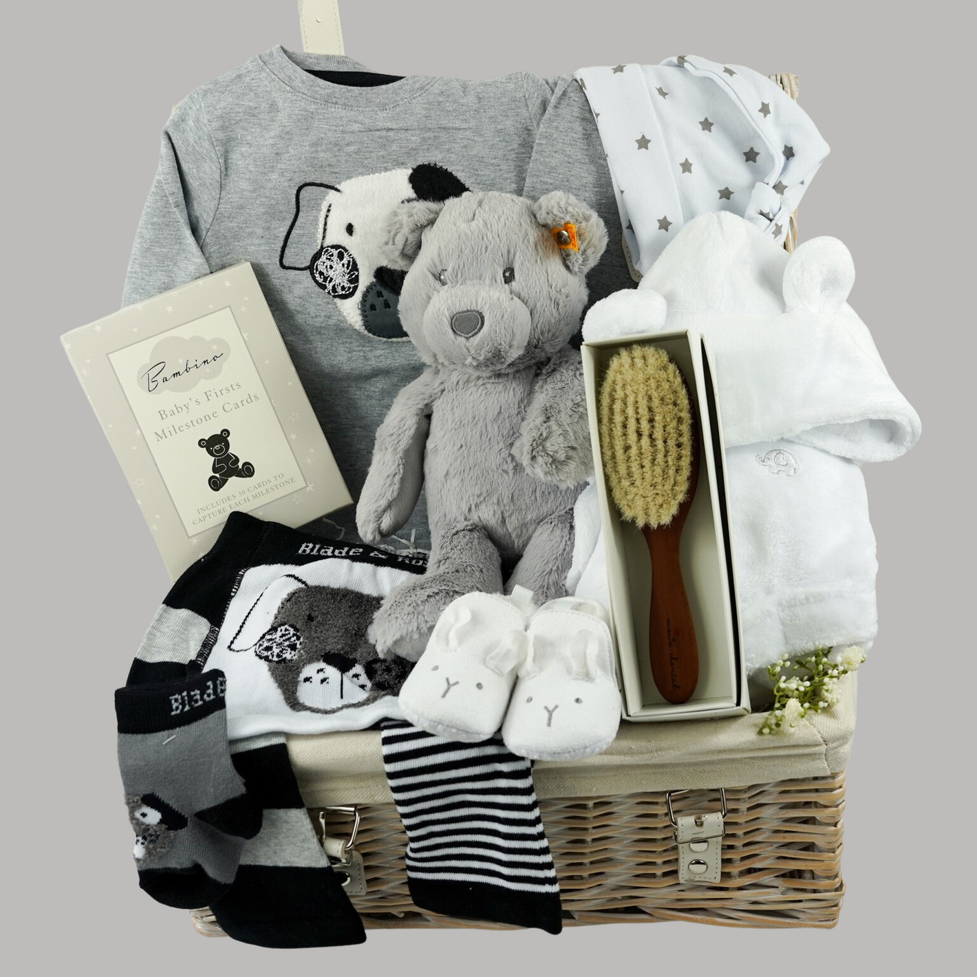 baby hamper basket with grey steiff teddy, grey and white 2 piece Blade and Rose outfit with a black and white dog, white baby slippers with ears, white baby dressing gown with ears , soft natural baby hairbrush, white with grey stars knot hat 