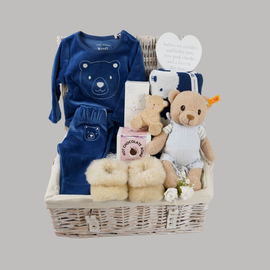 baby boy hamper with blue velour organic top and leggings, alpaca baby slippers, steiff organic bear, organic blue and white teddy bear blanket , wooden bear poush along toy , natural baby toiletries in a white wicker hamper basket