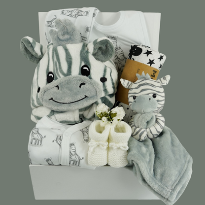 white hamper box with baby dressing gown with zebra faced hood, white baby sleepsuit with zebras, white baby hat with zebras, grey and white baby comforter with a zabra head, white knit baby booties, black and white sensory muslin swaddle  and 