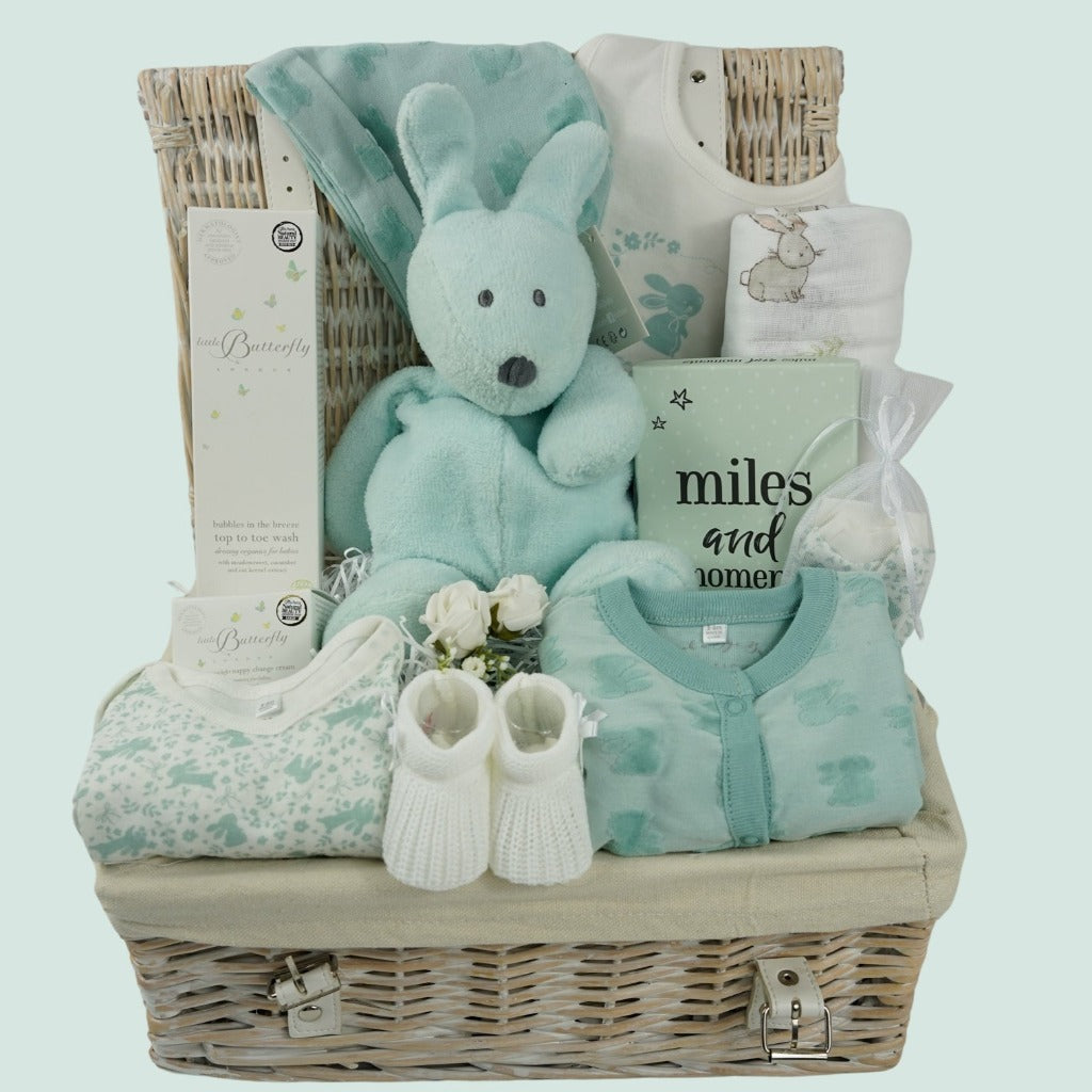 white hamper basket with mint green baby bunny soft toy by nattou, baby toiletries including bubble bath and nappy cream, green baby bunny layetter, bunny swaddle , boxed miles and moments baby milestone cards, white knit booties