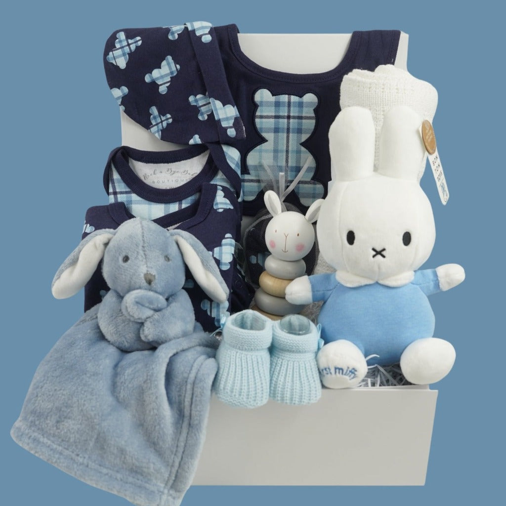 baby boy hamper includes navy baby layette with pale blue tartan teddy design includes a sleepsuit, bodysuit, hat, mittens and bib, white cotton cellular blanket, wooden rabbit stacking toy, dusky blue rabbit comforter, blue knit booties, My First Miffy white toy with a blue outfit