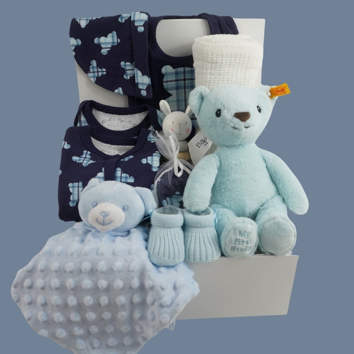 baby boy hamper includes blue layette baby clothing set in navy with tartan teddy pattern in lighter blue, blue knit booties, my first steiff teddy in blue with button in ear, wooden stacking toy, teddy dimple fleece baby comforter, white cellular blanket