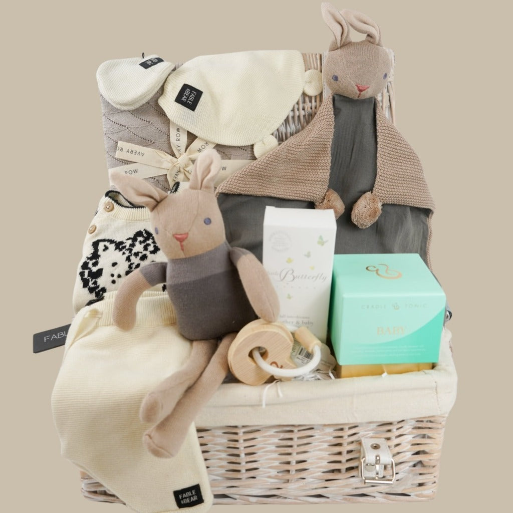 White wicker hamper basket, organic  baby rabbit toy and matching comforter, Knitted organic baby clothing set including a jumper  with leopard design, cradle and tonic baby candle, organic baby massage oil, wooden teething keys 