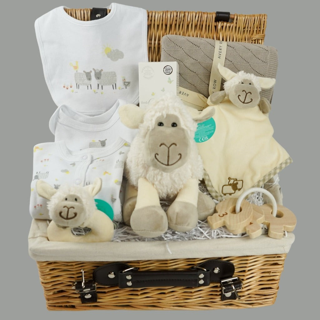 wicker hamper basket with white cotton baby clothing set with sheep design, organic baby blanket in buscuit colour, sheep soft toy, sheep rattle and sheep baby comforter finger puppet, wooden baby teether, organic baby wash