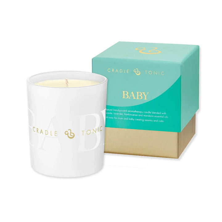 A white glass jar candle with a single wick and pale yellow wax, shown next to its mint green and gold Cradle of Tears Baby scented box on a white background.