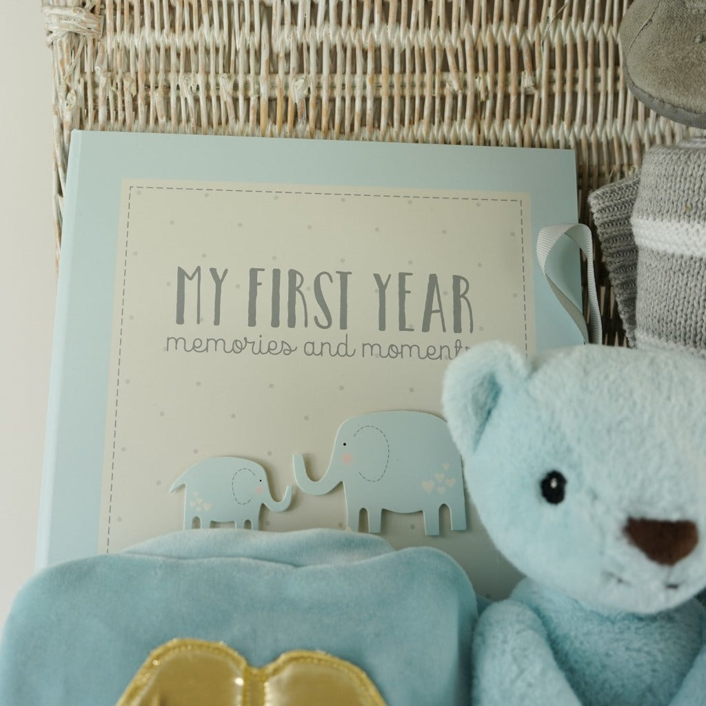White wicker basket, angel wings blue velour sleepsuit, blue Steiff my first teddy, grey and white ziggle blanket, My first year record book