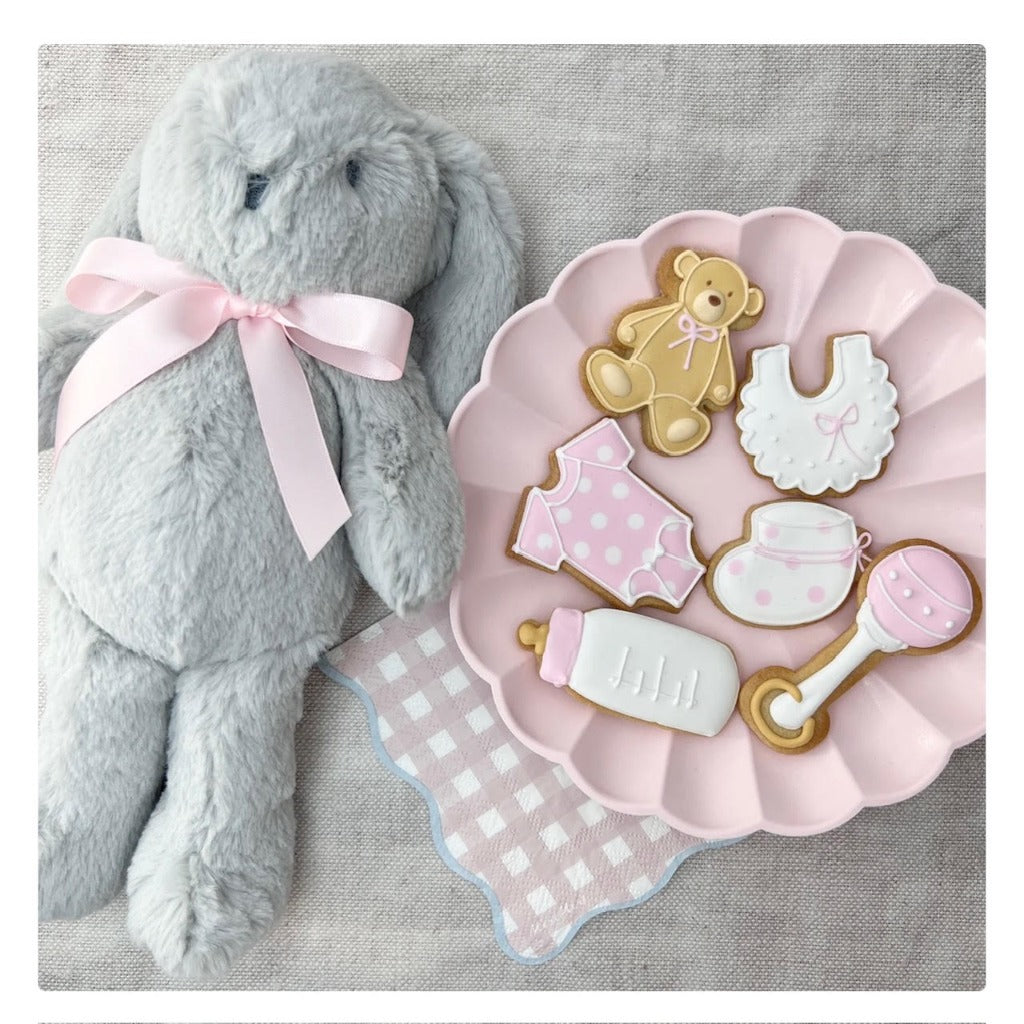 baby girl celebration biscuits in the shape of baby booties, rattle, bib, sleepsuit, teddy and baby bottle