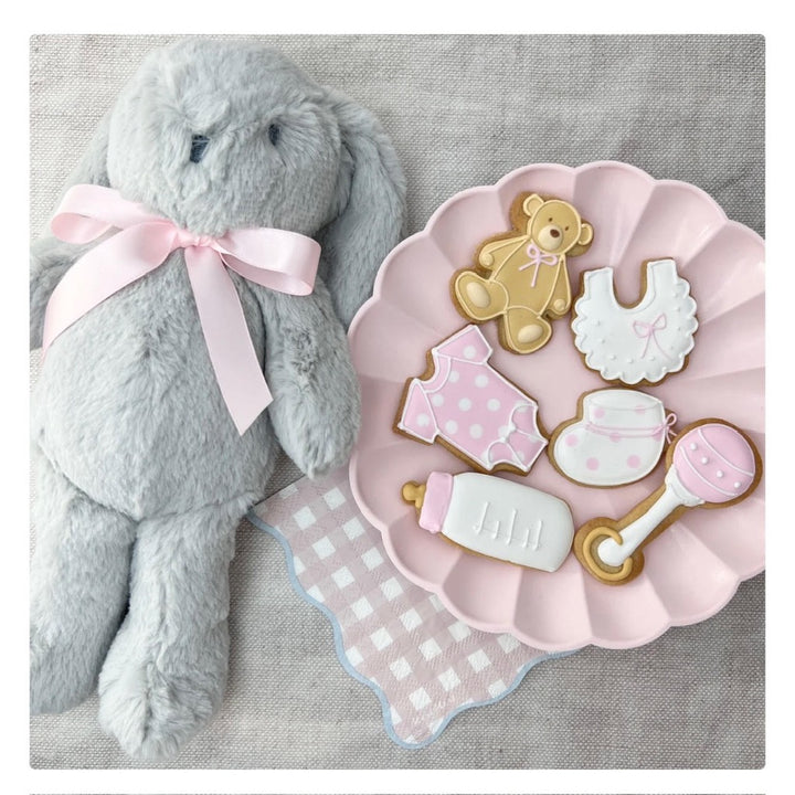 baby girl celebration biscuits in the shape of baby booties, rattle, bib, sleepsuit, teddy and baby bottle