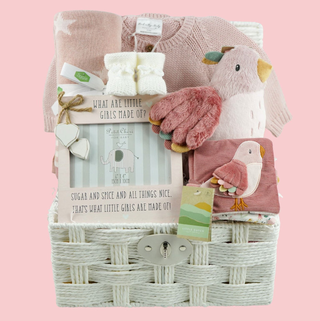 luxury baby girl hamper in mainly pink and white includes soft stroller book with a pink bird, butterflies and caterpillar theme, pink bird soft toy, white knit baby booties, dusky pink reversible baby blanket and pink baby girl picture frame and a pink baby girl cardigan in a white paper rope hamper basket