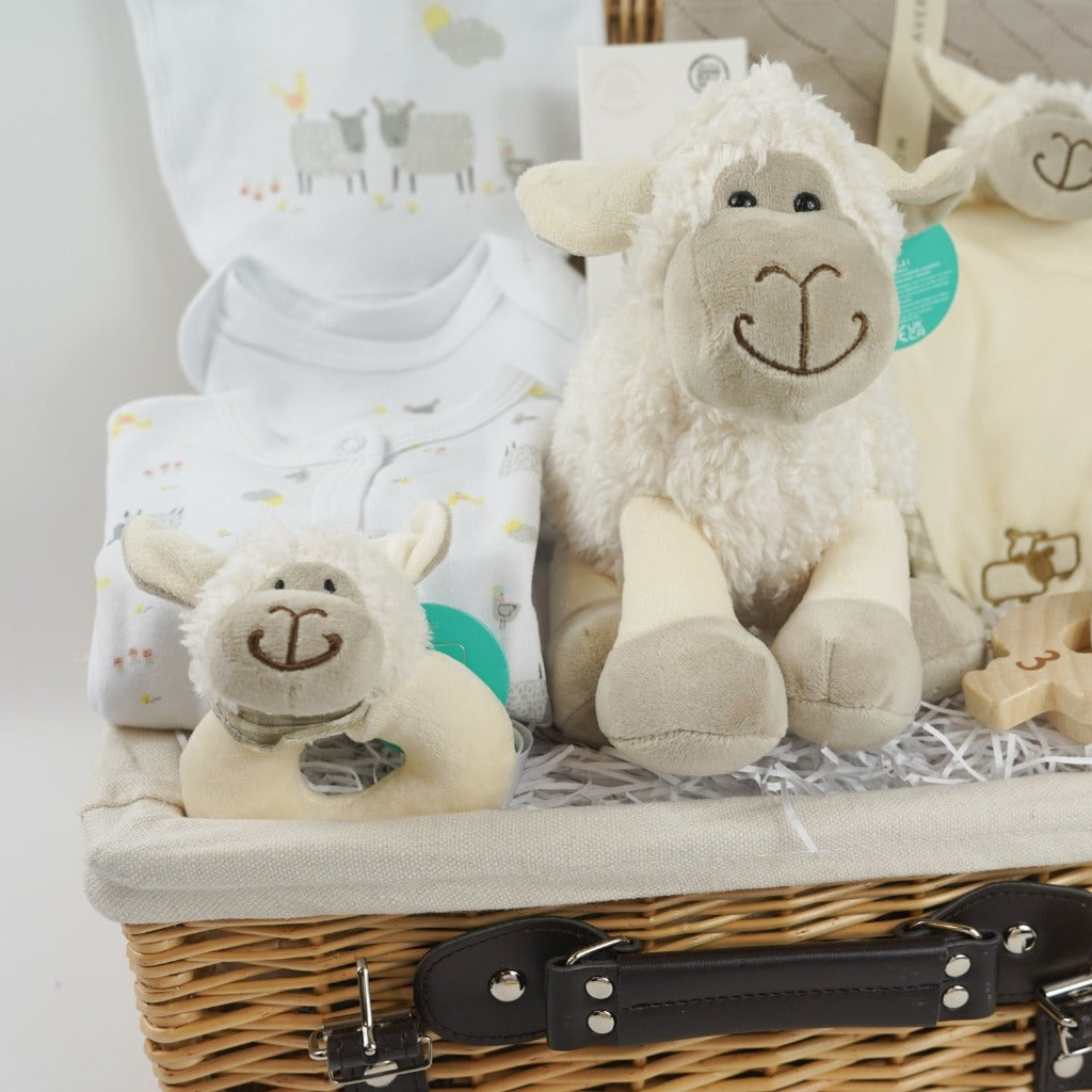 wicker hamper basket with white cotton baby clothing set with sheep design, organic baby blanket in buscuit colour, sheep soft toy, sheep rattle and sheep baby comforter finger puppet, wooden baby teether, organic baby wash