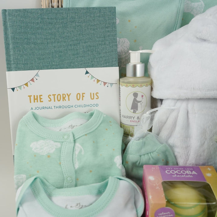 baby hamper basket, baby journal, baby layette outfit in pale mint green with elephants , white baby dressing gown with cute ears, white hot chocolate bomb, baby organic bubble bath, Dragon taggie in green and matching taggie book , white knit booties