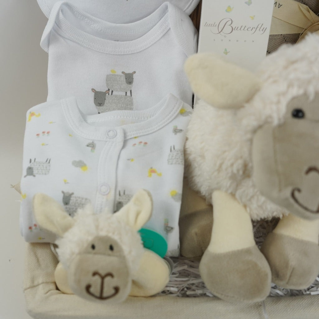 wicker hamper basket with white cotton baby clothing set with sheep design, organic baby blanket in buscuit colour, sheep soft toy, sheep rattle and sheep baby comforter finger puppet, wooden baby teether, organic baby wash