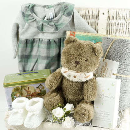 Wicker hamper basket with Calamaro grey and gren check baby romper, brown soft baby teddy bear, baby white booties, Alice in Wonderland tea caddy, grey cellular baby blanket, messages for you baby keepsake book, little butterfly London baby and mum toiletries