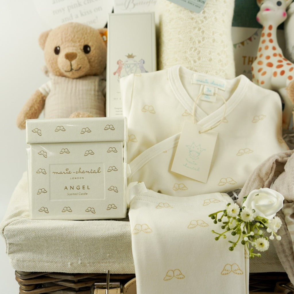 Luxury baby gifts in a hamper basket, Luxury New Mum candle , Angel Wings 2 piece baby clothing set in cream with gold angel wing design, baby hairbrush, baby cashmere shawl, sophie la giraffe, organic steiff teddy and comforter, baby jourmal , baby slippers and baby swaddle in white with grey safari animals