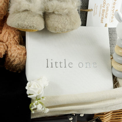 baby hamper basket with honey coloured steiff teddy, baby alpaca slippers in champagne, baby knitted jumper in organic cream cotton with black leopard design, black baby cotton knitted leggings, black cotton knit baby hat with ears, baby photo album in white linen, baby stacking ring toy with rabbit head, grey cotton baby cellular blanket