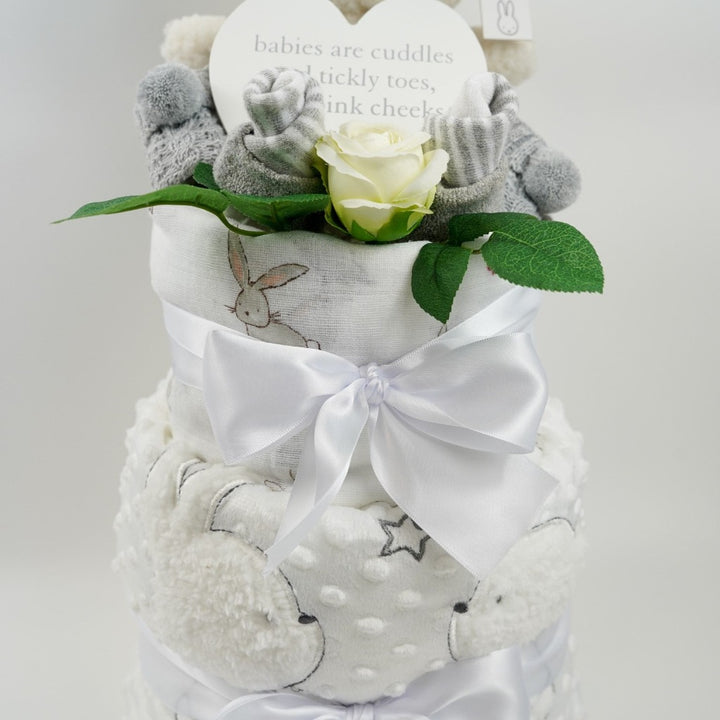 baby cake with grey striped socks, baby bootees in grey with pom poms, white dimpled blanket with sherpa backing with a bunny and teddy applique, white swaddle with bunnies, cream teddy , white plaque for the nursery