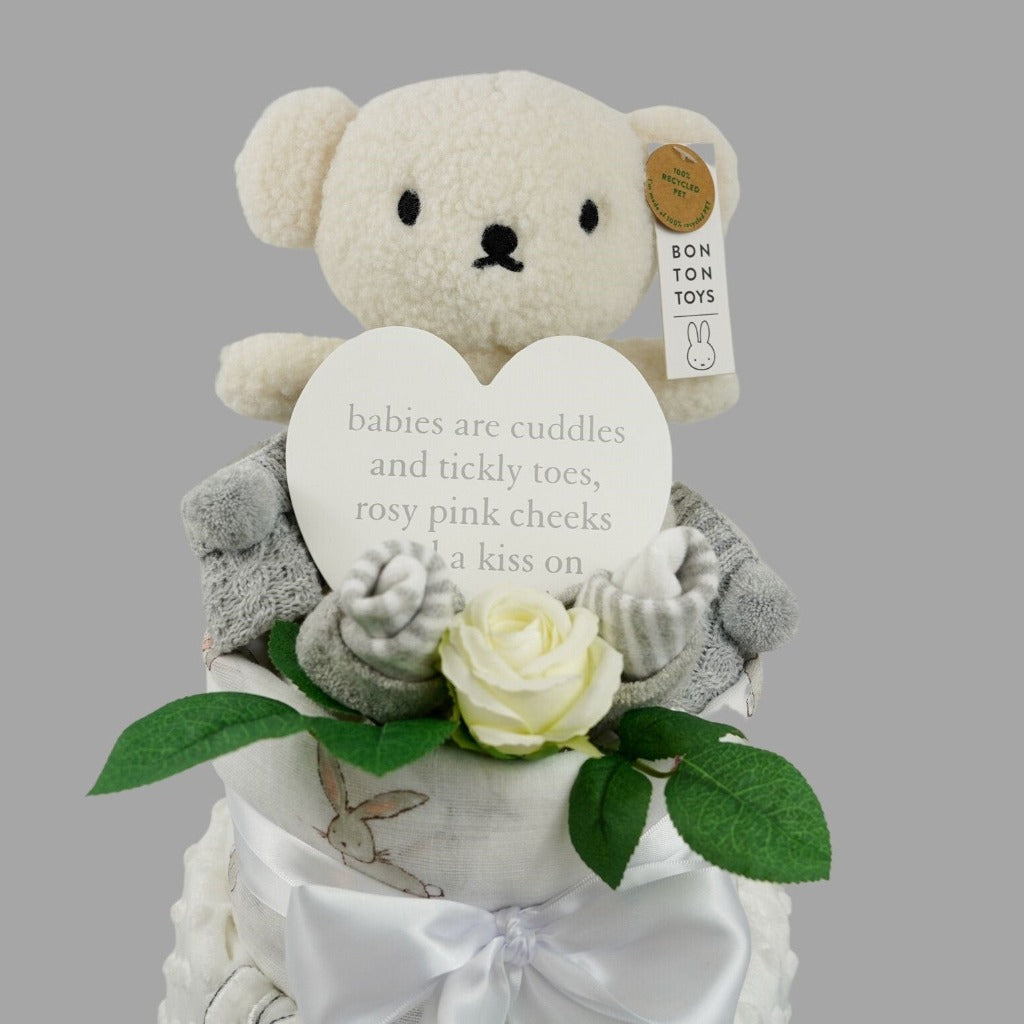 baby cake with grey striped socks, baby bootees in grey with pom poms, white dimpled blanket with sherpa backing with a bunny and teddy applique, white swaddle with bunnies, cream teddy , white plaque for the nursery