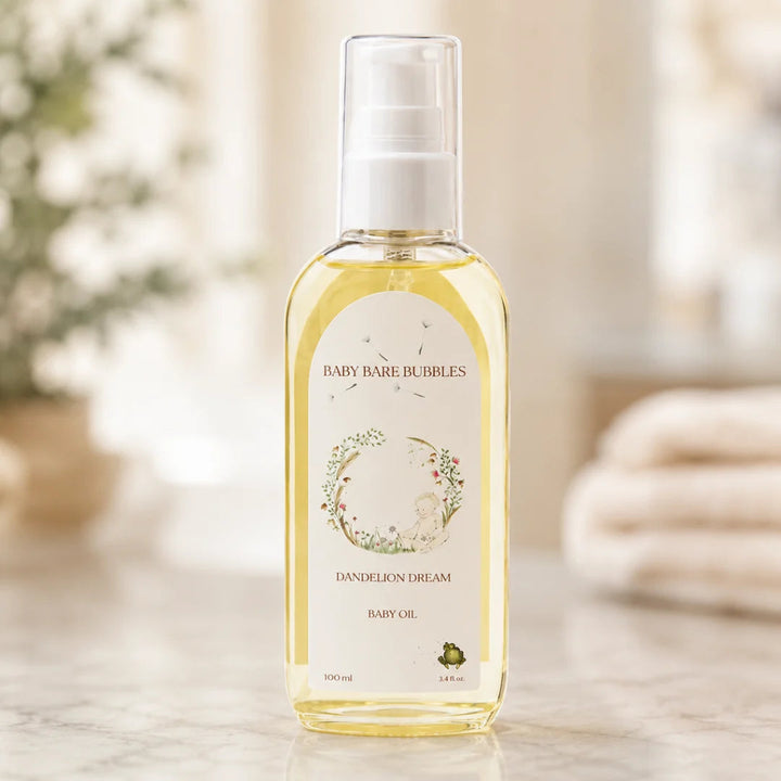 A bottle of Baby Bare Bubbles Dandelion Dream Baby Oil on a marble surface with a soft, blurred bathroom background.