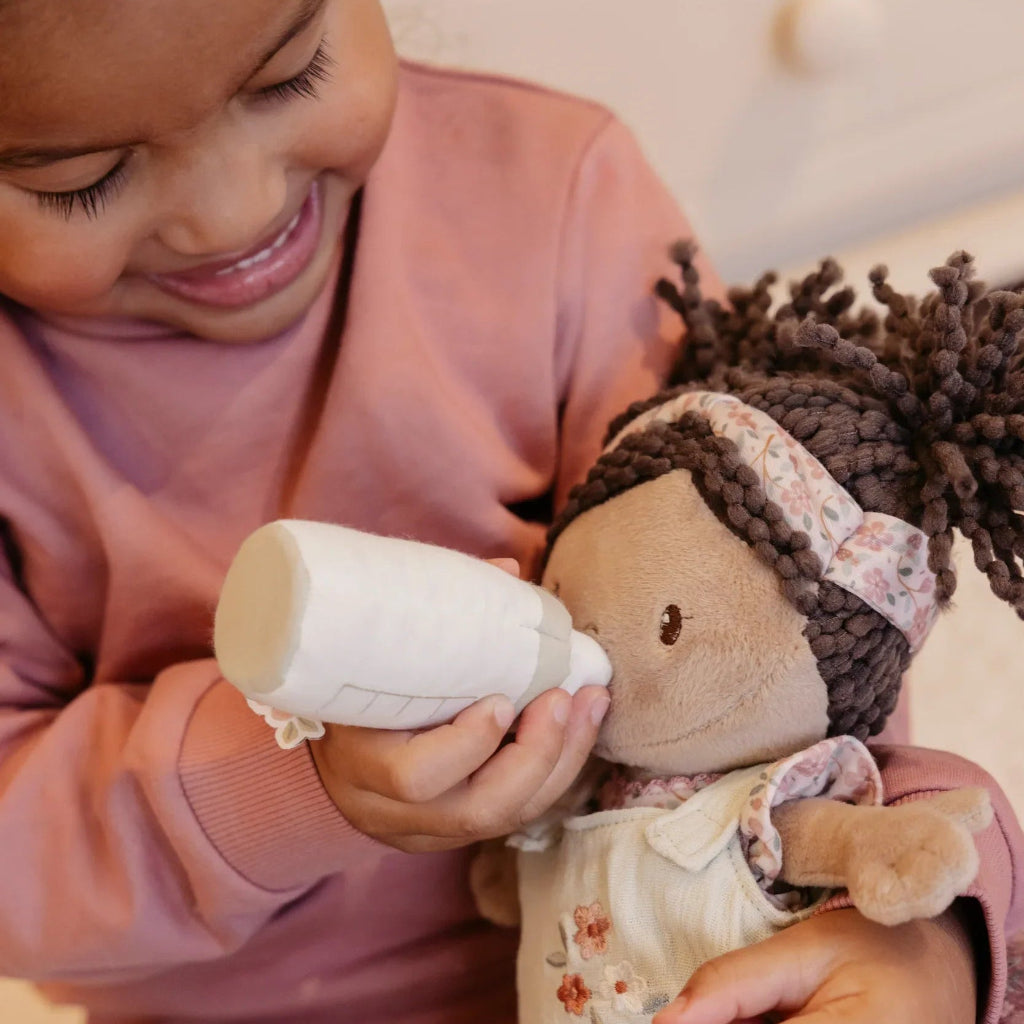soft baby doll in a green fabric basket with a dummy, bottle and sleeping bag 