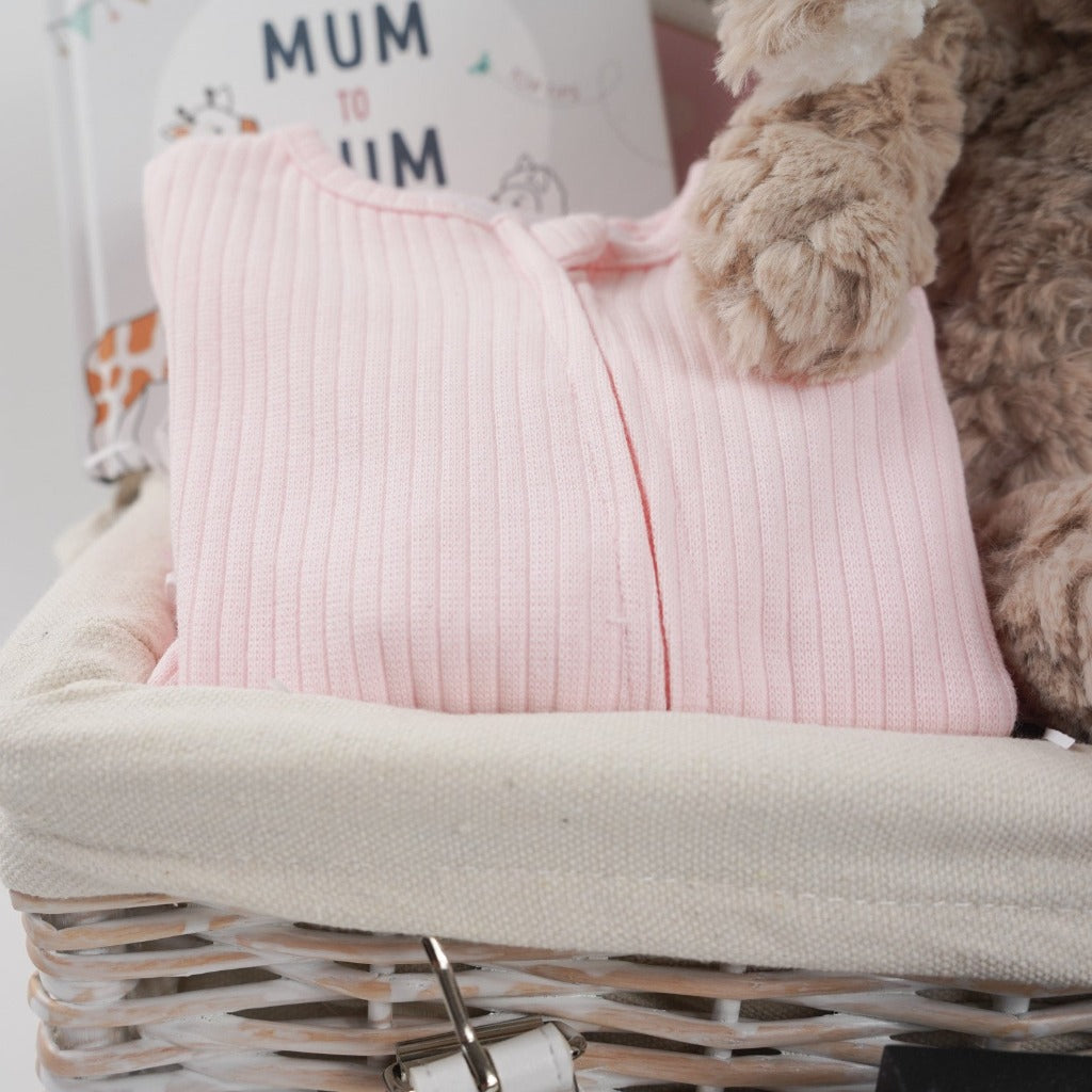 white wicker hamper basket with mum to be gifts includes box with toiletries for mum and baby, mum to mum advice book, pale pink ribbed baby sleepsuit with zip fastening, soft carmel coloured bunny rabbit soft toy, dusky pink heavy weight baby blanket with stars, bump pregnancy candle