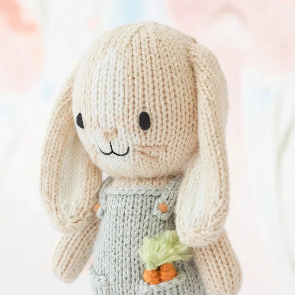Knitted toy rabbit with a carrot in his pocket and light blue dungarees
