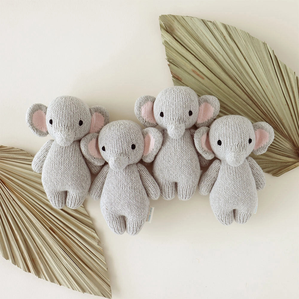 Four knitted elephant toys on a light background with decorative leaves.