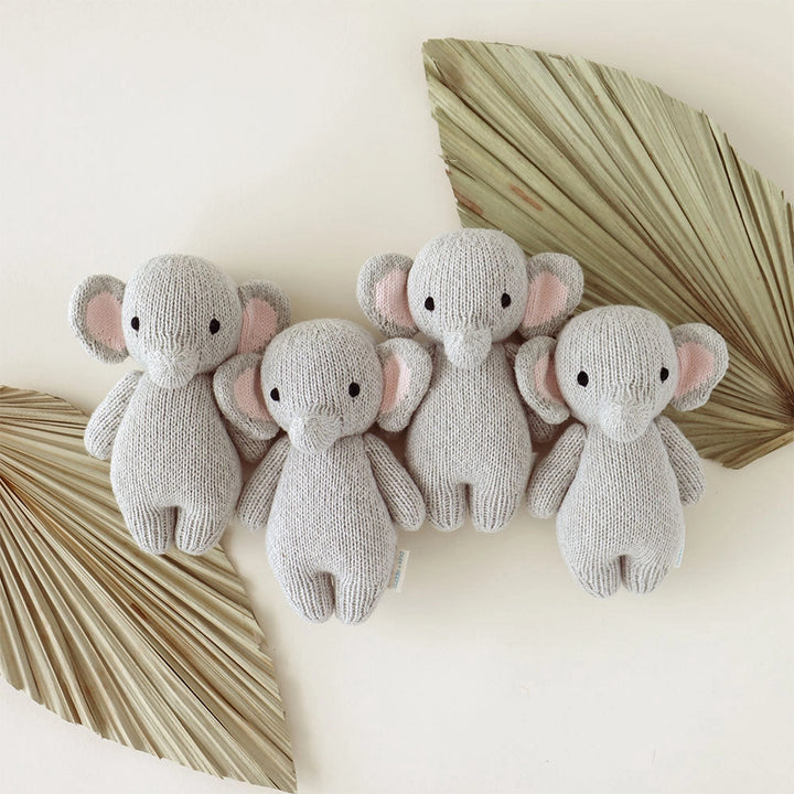 Four knitted elephant toys on a light background with decorative leaves.