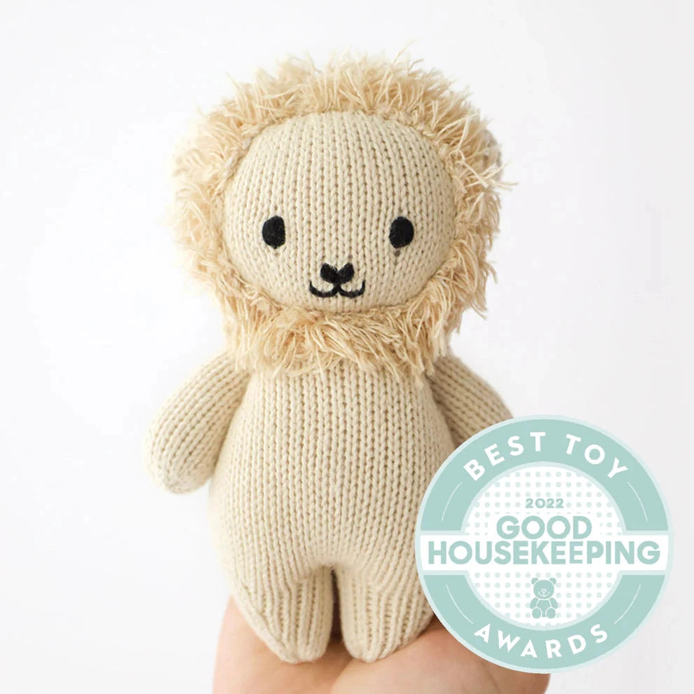 Knitted lion toy held by a hand with Good Housekeeping Award badge.
